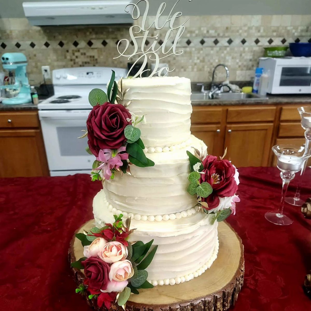 Three-tiered white cake with red roses and a We Still Do topper.
