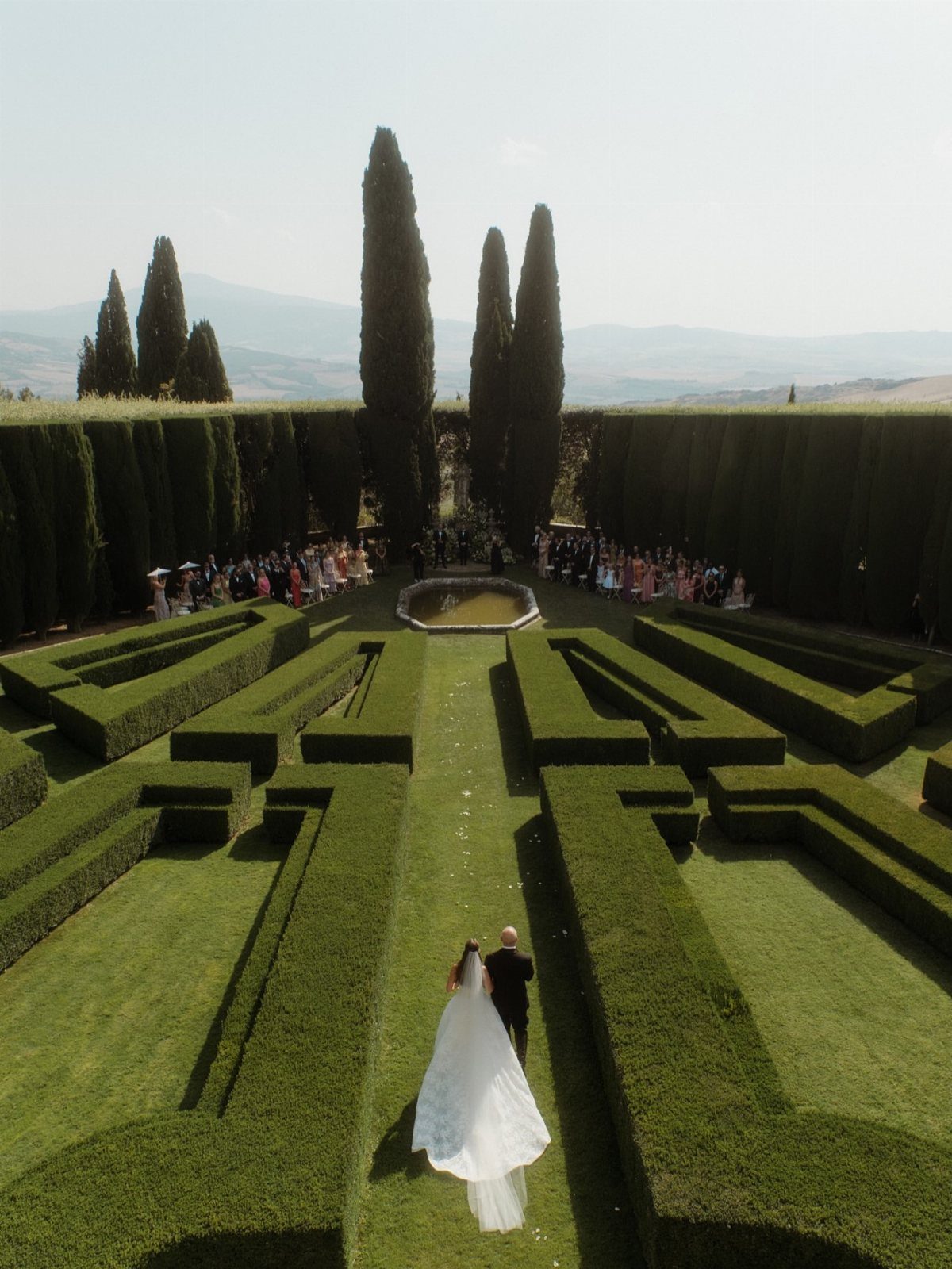 Bride and groom walking through a geometric Italian garden with tall cypress trees