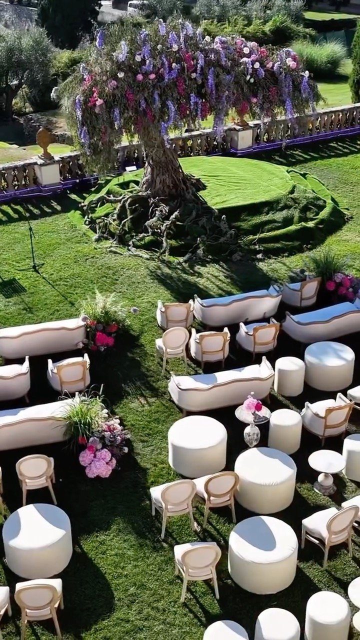 White luxury lounge furniture arranged on a lawn under a flower-decorated tree.