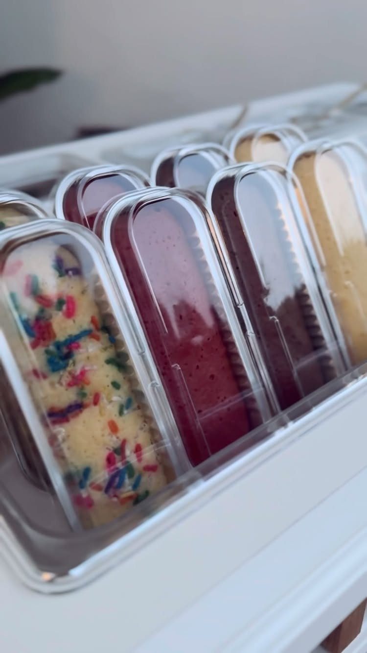 Assorted colorful popsicles in clear plastic wrappers arranged in a white tray.