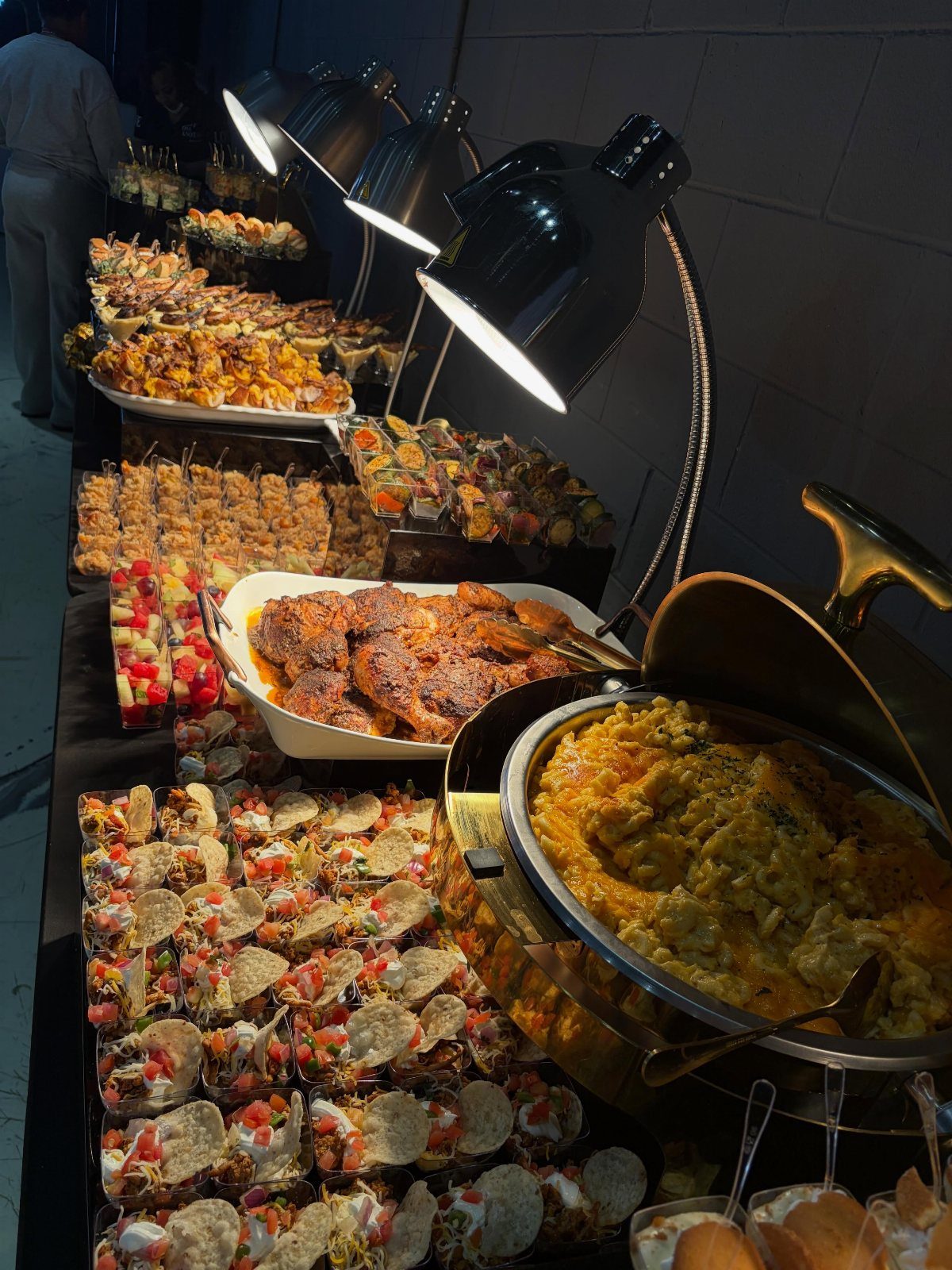Assorted appetizers and a chafing dish on a catering table under heat lamps.