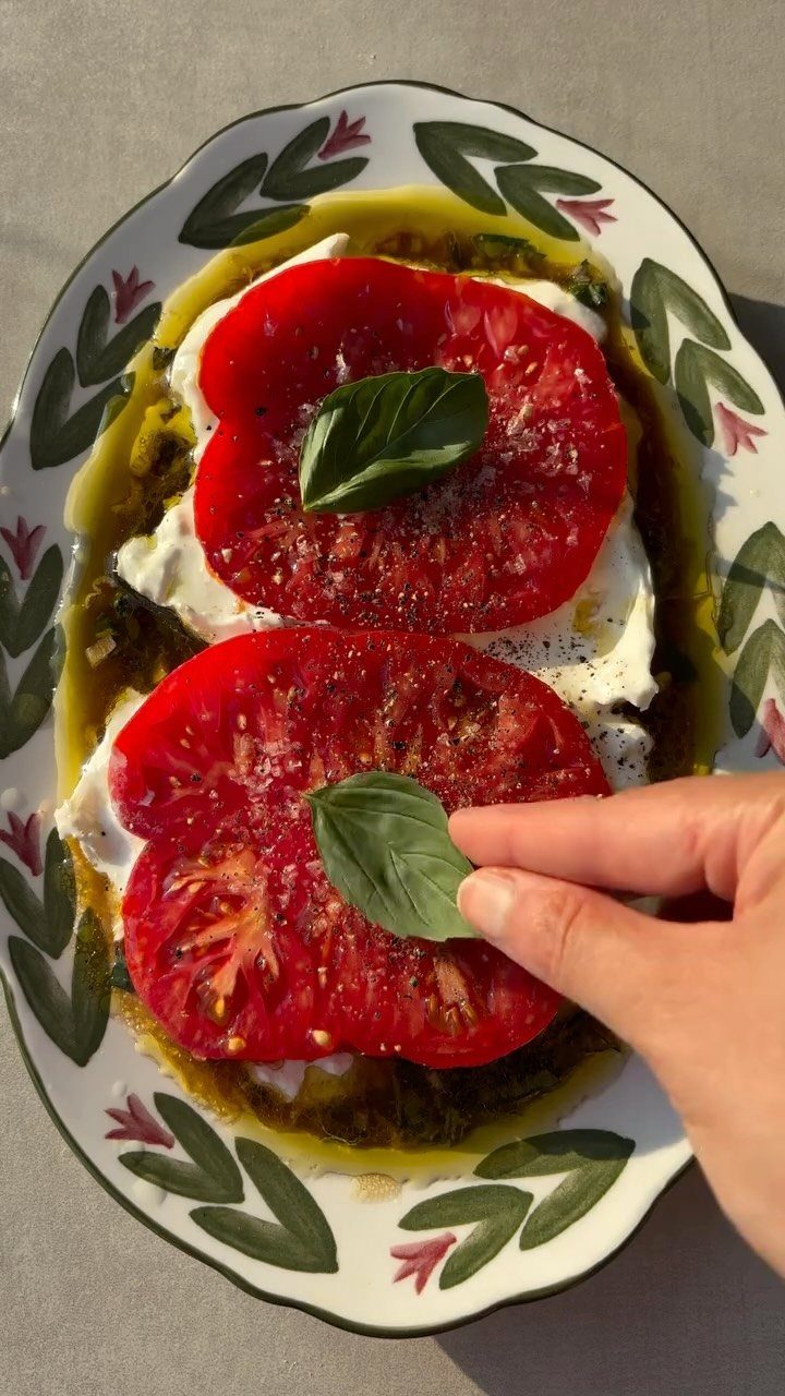 Heirloom tomato and burrata salad with basil leaves on a decorative plate.