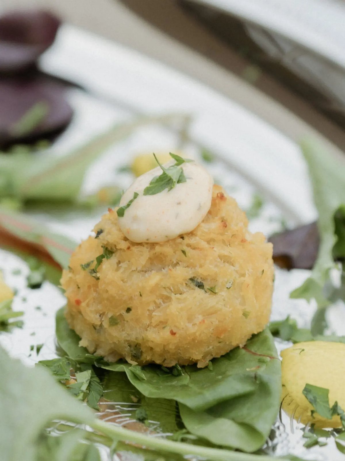 Mini crab cake topped with white sauce on a spinach leaf platter