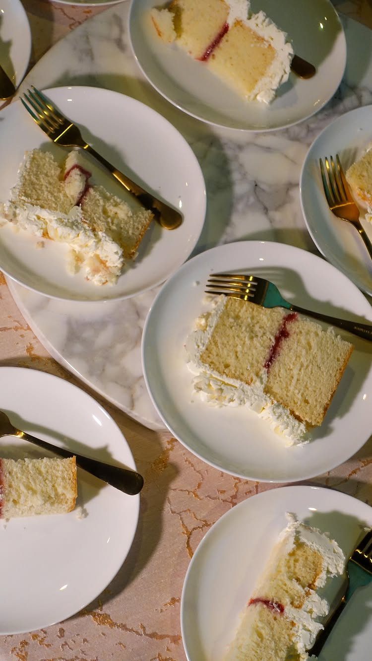 Slices of white layer cake with jam on white plates with gold forks.