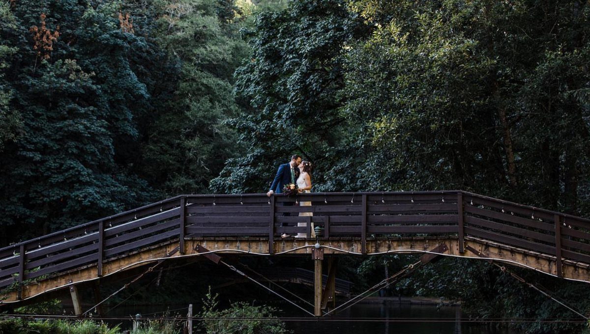 Bride and groom kissing on a wooden bridge over a creek in forest