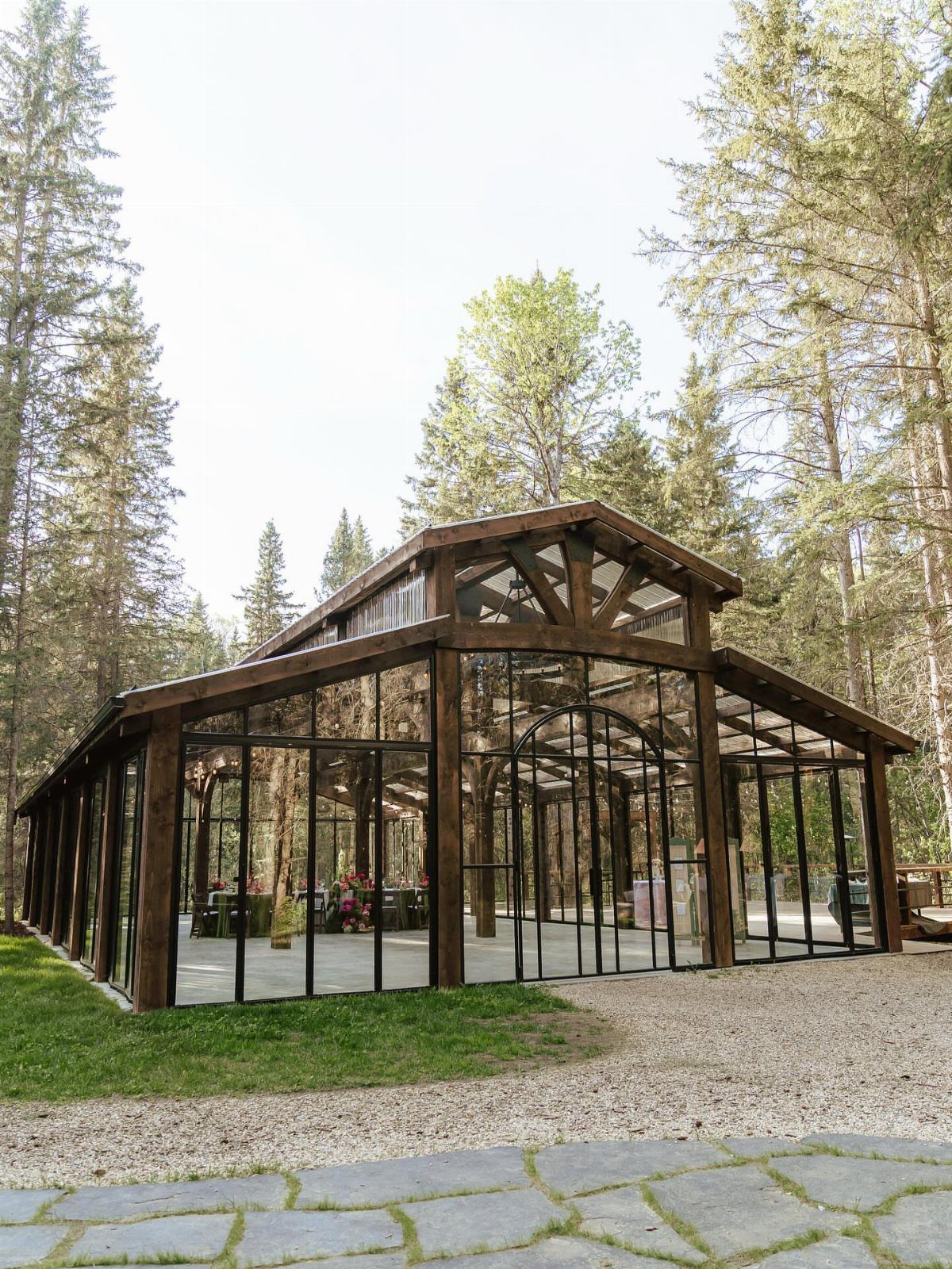 Glass-walled wooden pavilion wedding venue surrounded by tall evergreen forest trees