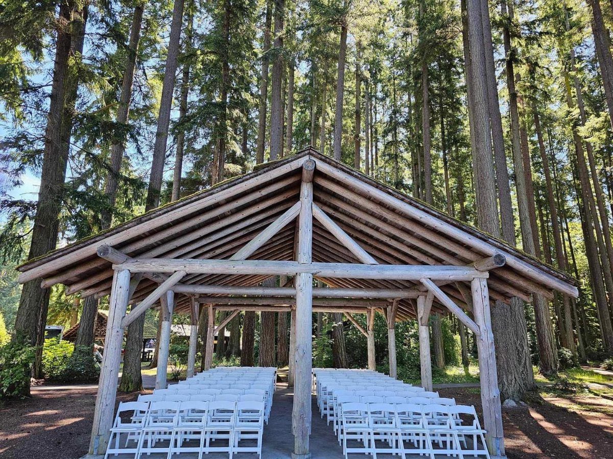 Wooden open-air pavilion with white chairs set in a tall evergreen forest
