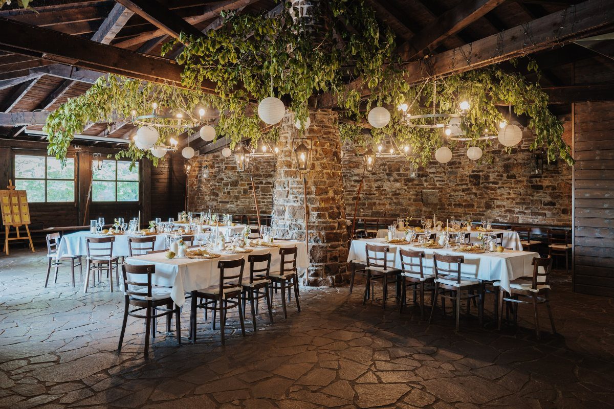 Rustic indoor event space with stone walls, white clothed tables, and hanging greenery.