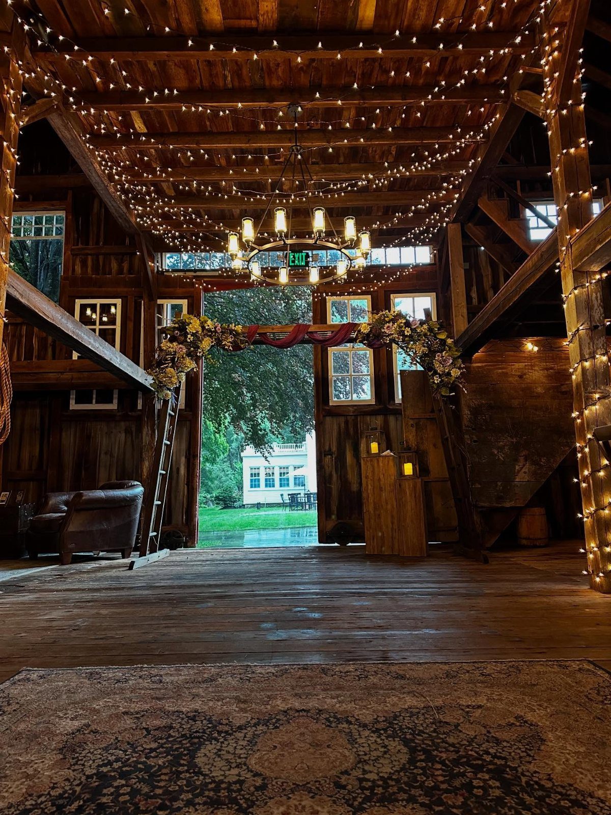 Rustic wooden barn interior with string lights and floral arch overlooking a lawn