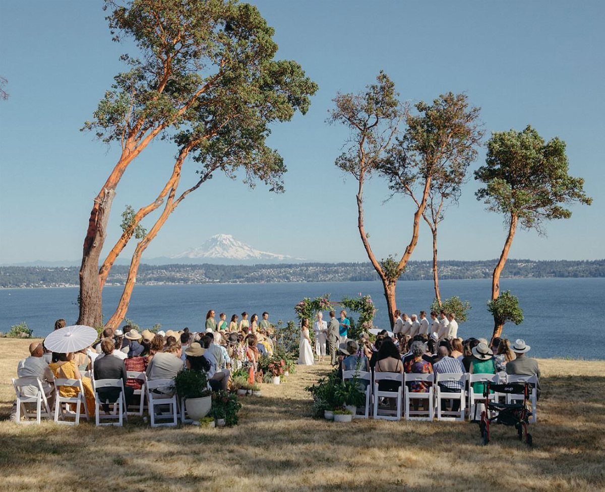 Wedding ceremony on a grassy cliff overlooking a lake and snow-capped mountain peak.