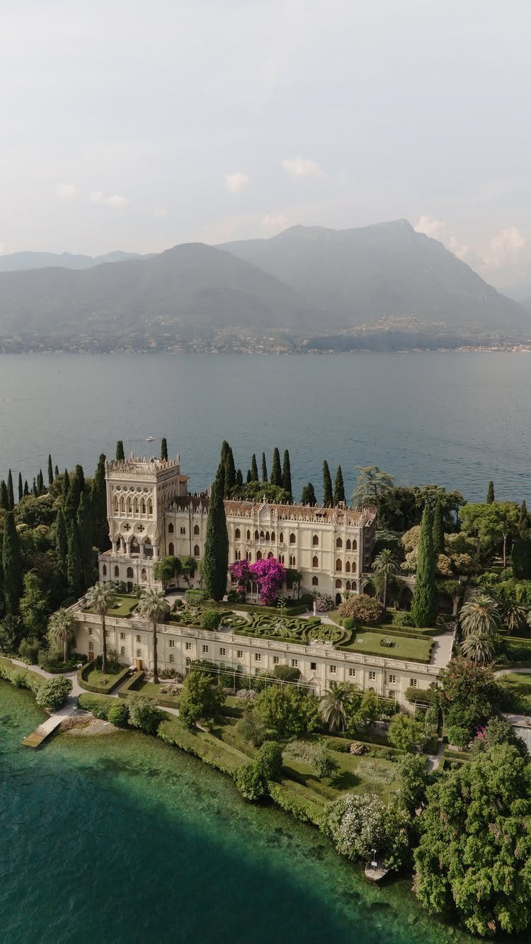 Grand stone villa with gardens on a lake shore with distant mountains.