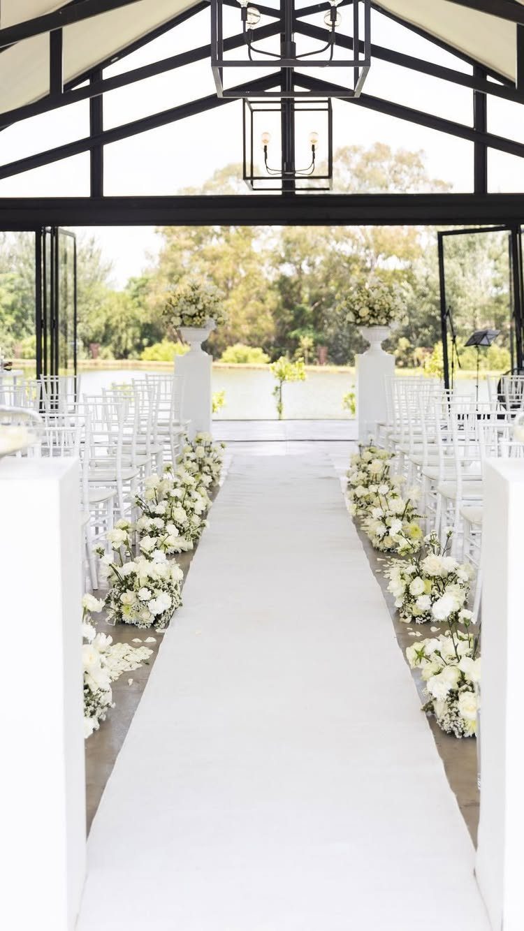 Wedding ceremony aisle with white flowers and chairs overlooking a calm lake.