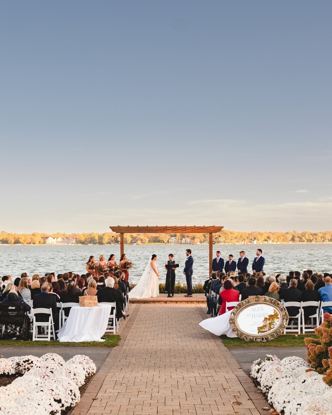 Wedding ceremony by a lake with a couple under a wooden pergola.