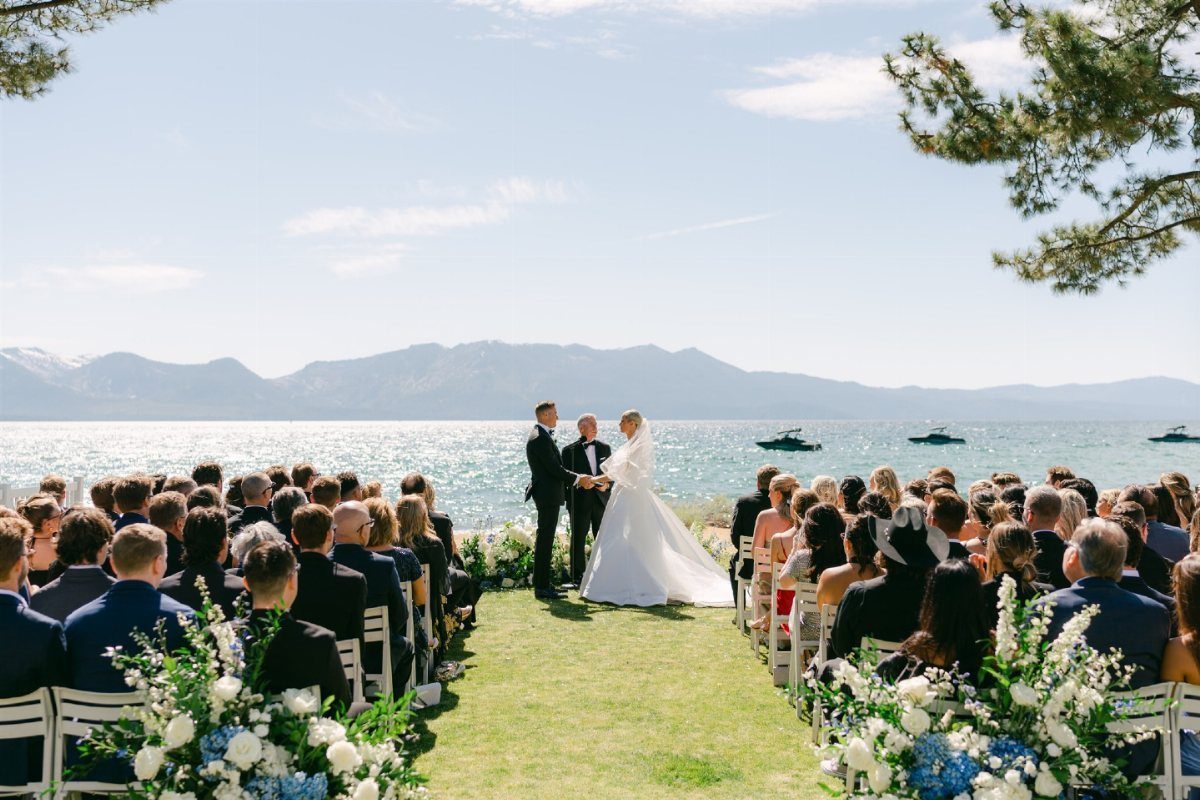 Wedding ceremony on a grassy lawn overlooking a large lake and distant mountains.