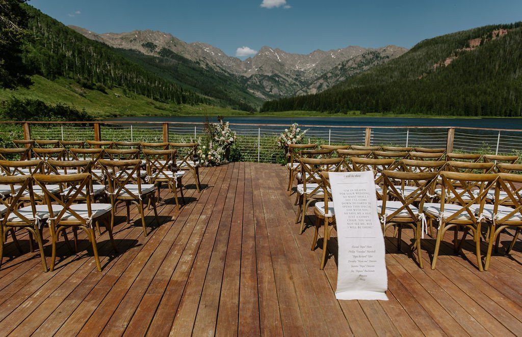 Wooden wedding ceremony chairs on a deck overlooking a lake and mountains.