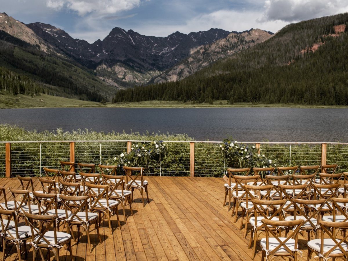 Wooden wedding ceremony deck with chairs overlooking a lake and rugged mountains.
