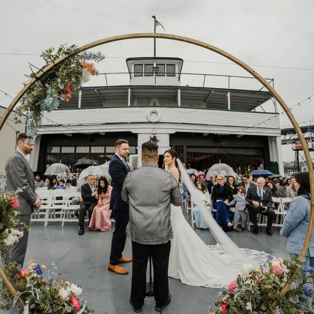 Wedding ceremony on a white wooden ferry boat deck with a floral arch.