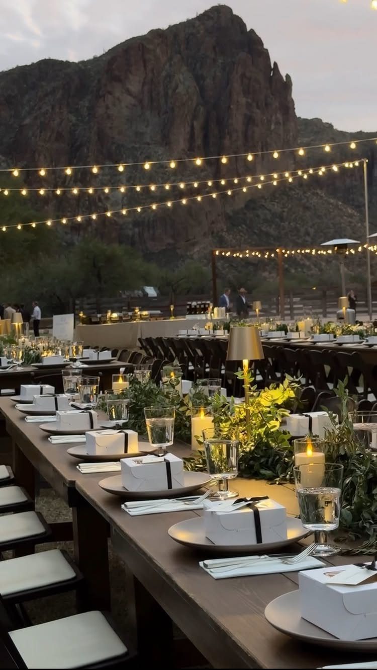 Outdoor wedding reception tables with string lights and a rocky desert mountain backdrop.