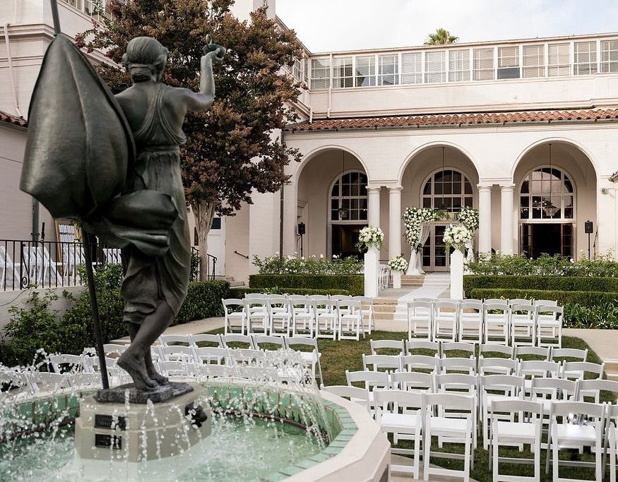 White wedding chairs arranged on a lawn before a historic arched building.