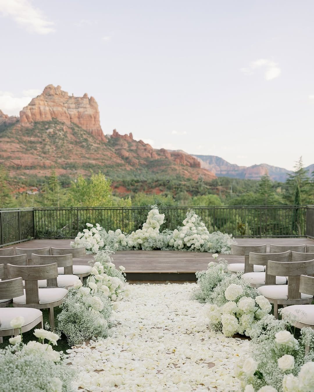 Outdoor wedding ceremony setup with white flowers and red rock mountain views.