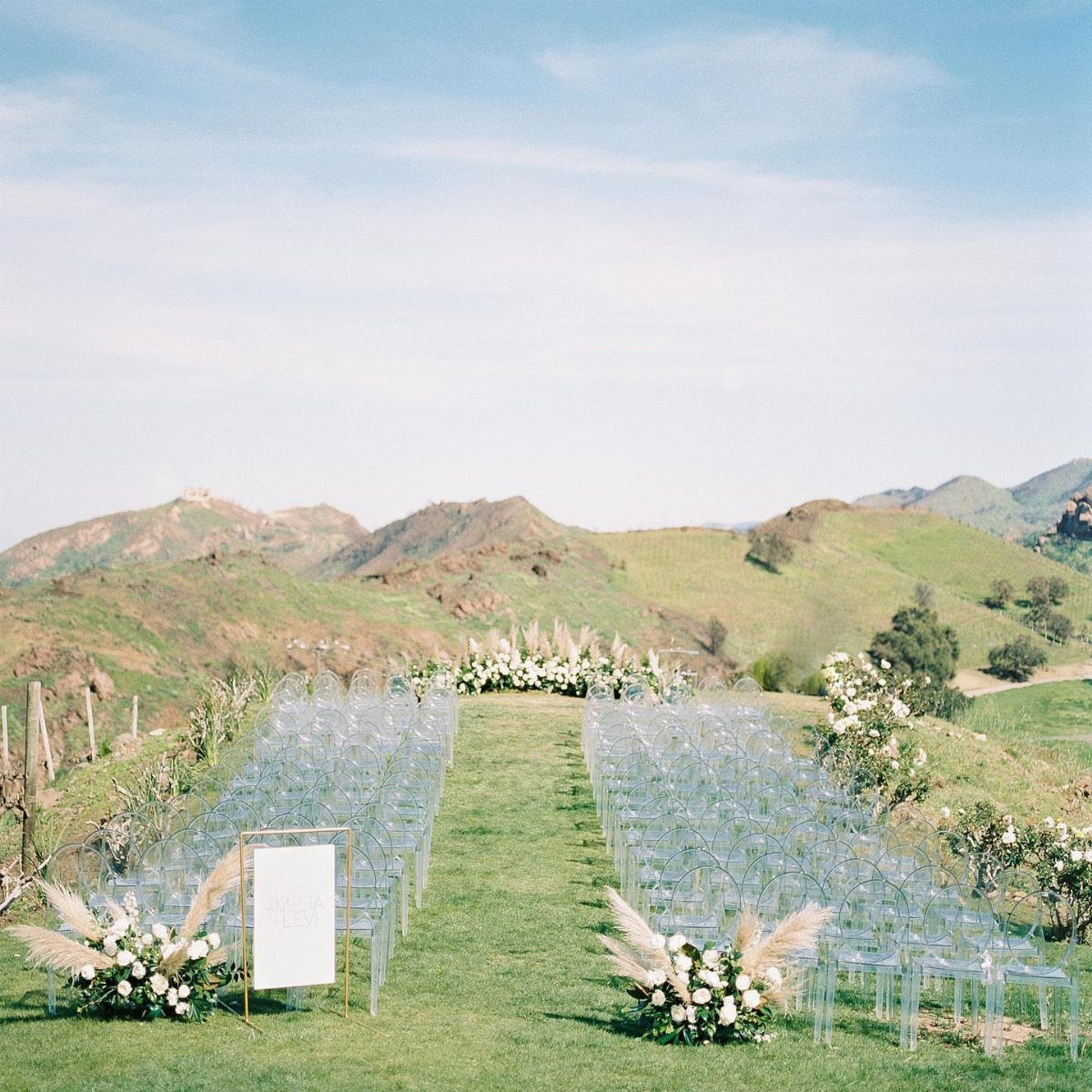 Outdoor wedding ceremony setup with clear chairs overlooking a panoramic mountain landscape.