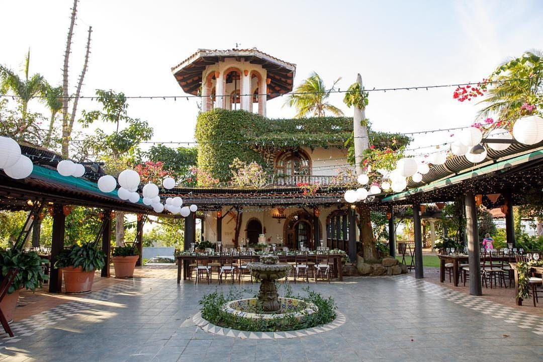 Stone tiered fountain on a patio with dining tables and Mediterranean architecture.
