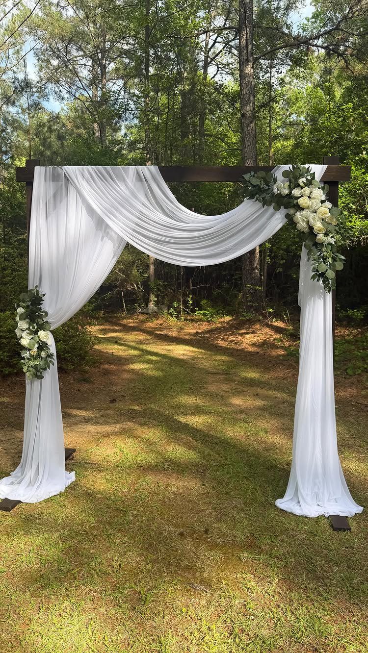 Wooden wedding arch with white fabric and flowers on a grassy lawn
