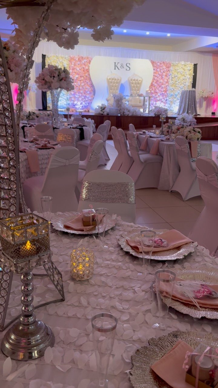 Wedding reception hall with white chairs, pink table settings, and a floral backdrop.