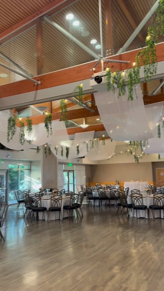 Event space with round tables, white linens, and hanging greenery under wooden beams.