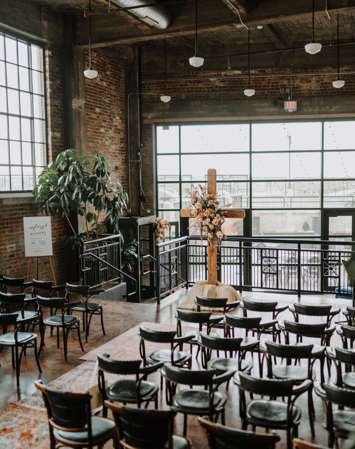 Industrial wedding venue with black chairs and a floral wooden cross altar.