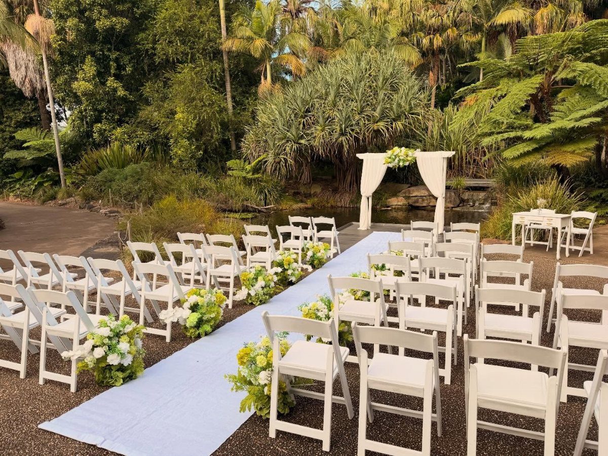 White folding chairs and a floral aisle leading to an arch in a garden
