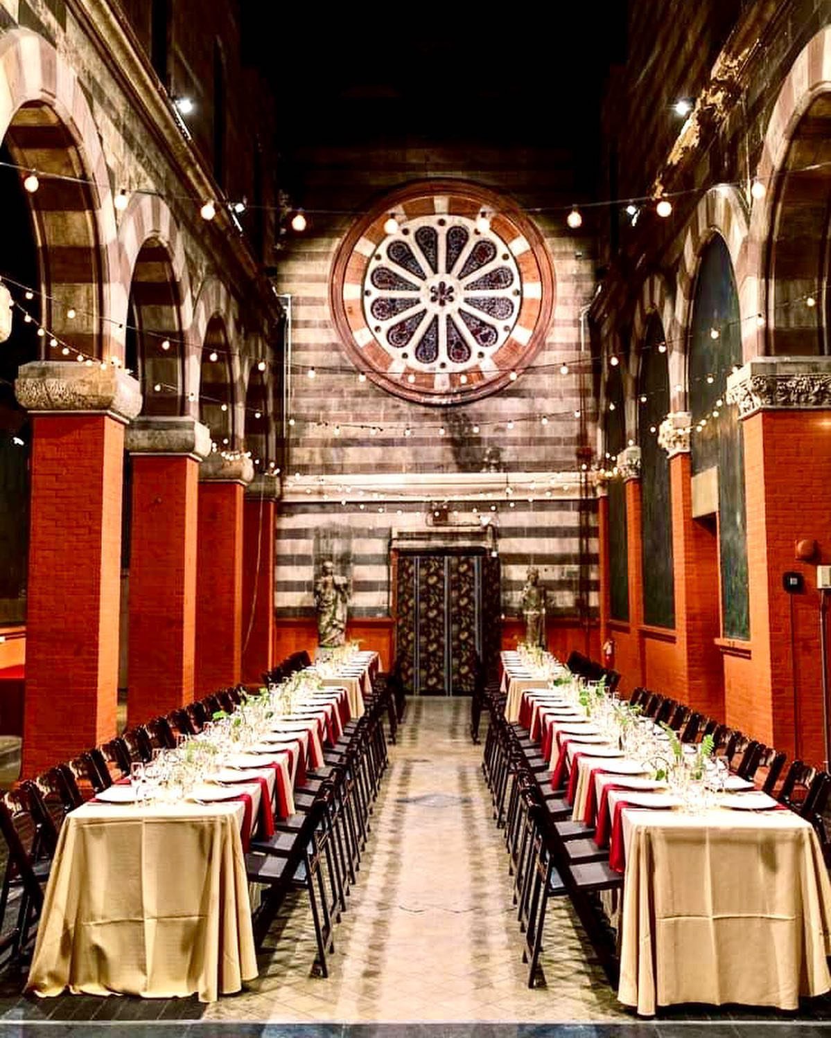 Long banquet tables set for a wedding in a grand hall with rose window.