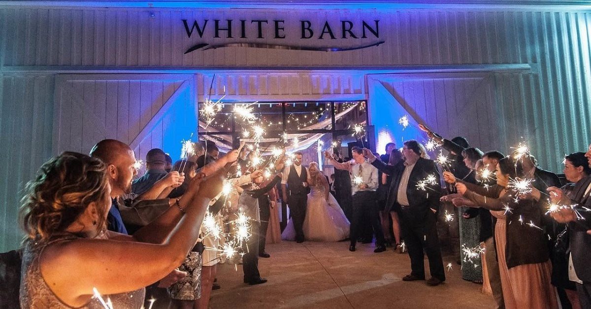Wedding couple walking through a sparkler send-off in front of a white barn venue.