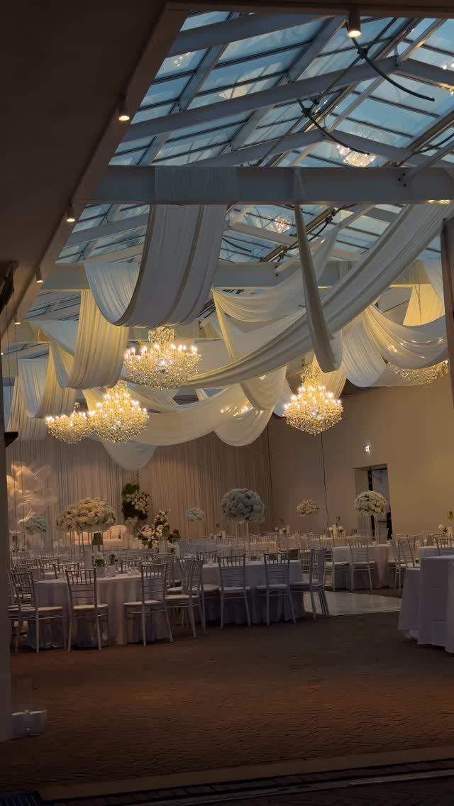 White fabric ceiling drapes and crystal chandeliers over wedding reception tables and chairs