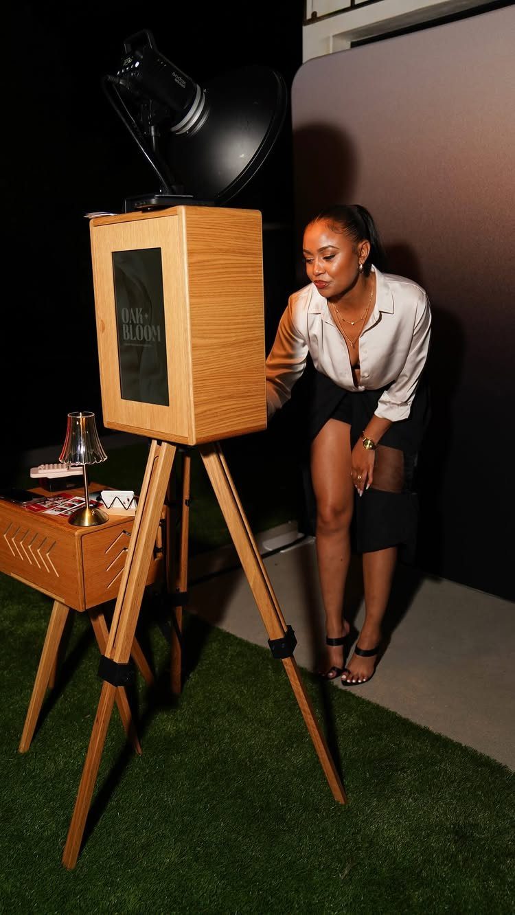 Wooden photo booth on a tripod with a woman standing beside it.