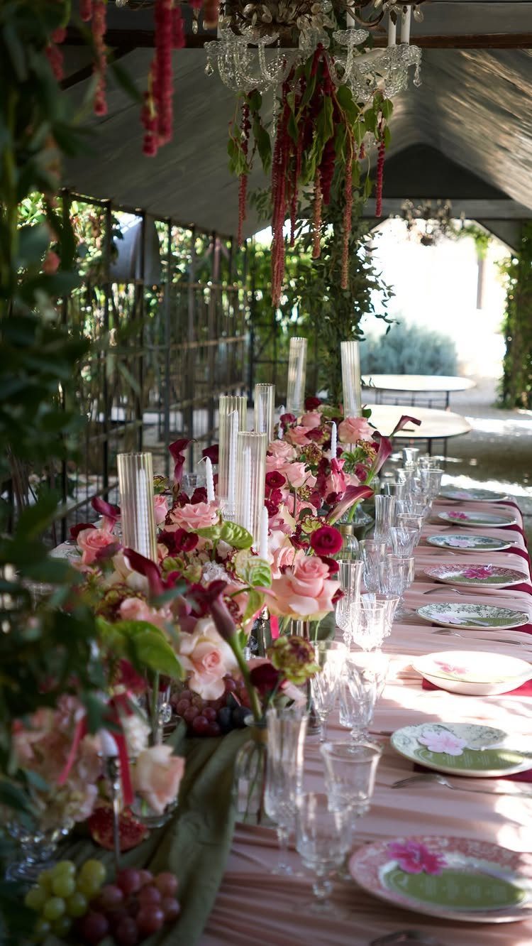 Long dining table with pink floral arrangements and red flowers hanging from above