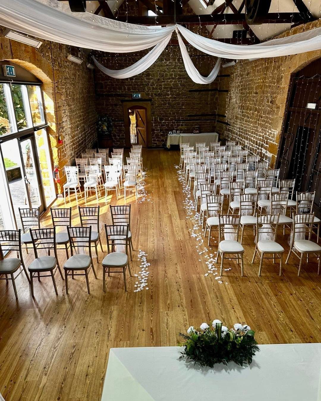 Ceremony setup with white chairs and flower petals in a rustic brick venue.